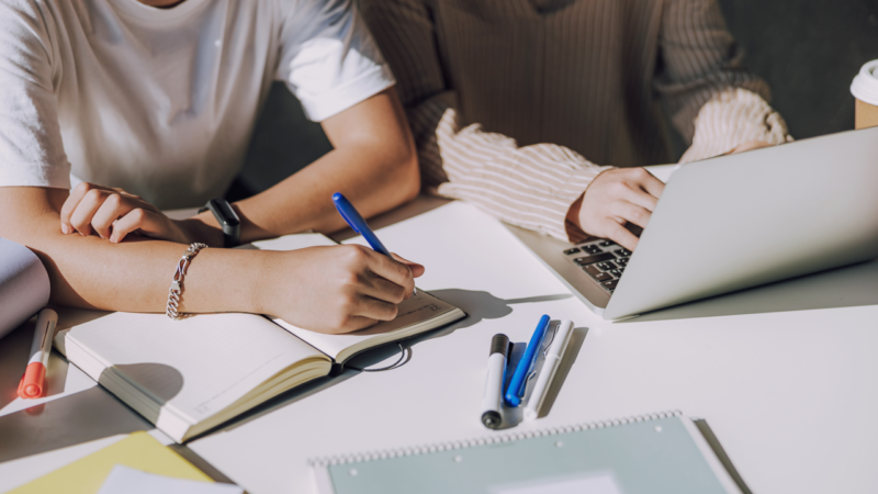 Deux personnes travaillent ensemble à un bureau, prenant des notes et utilisant un ordinateur portable dans un environnement professionnel collaboratif.