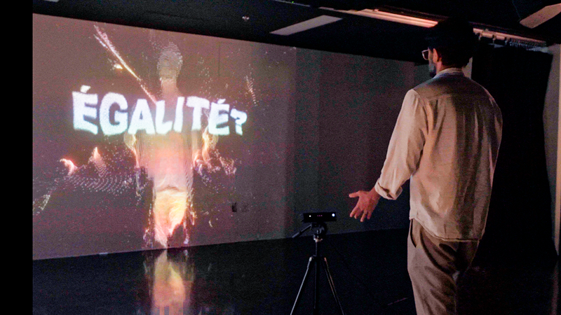 Une personne interagit avec un capteur de mouvement devant une projection du mot « égalité?».